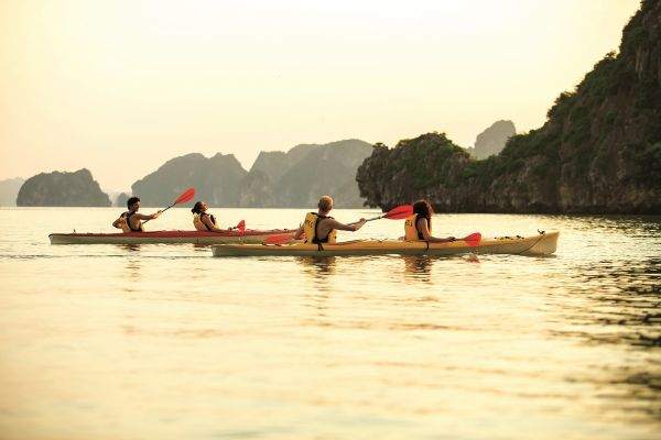 Touristen paddeln mit dem Kajak bei Sonnenuntergang in der Ha Long Bucht.